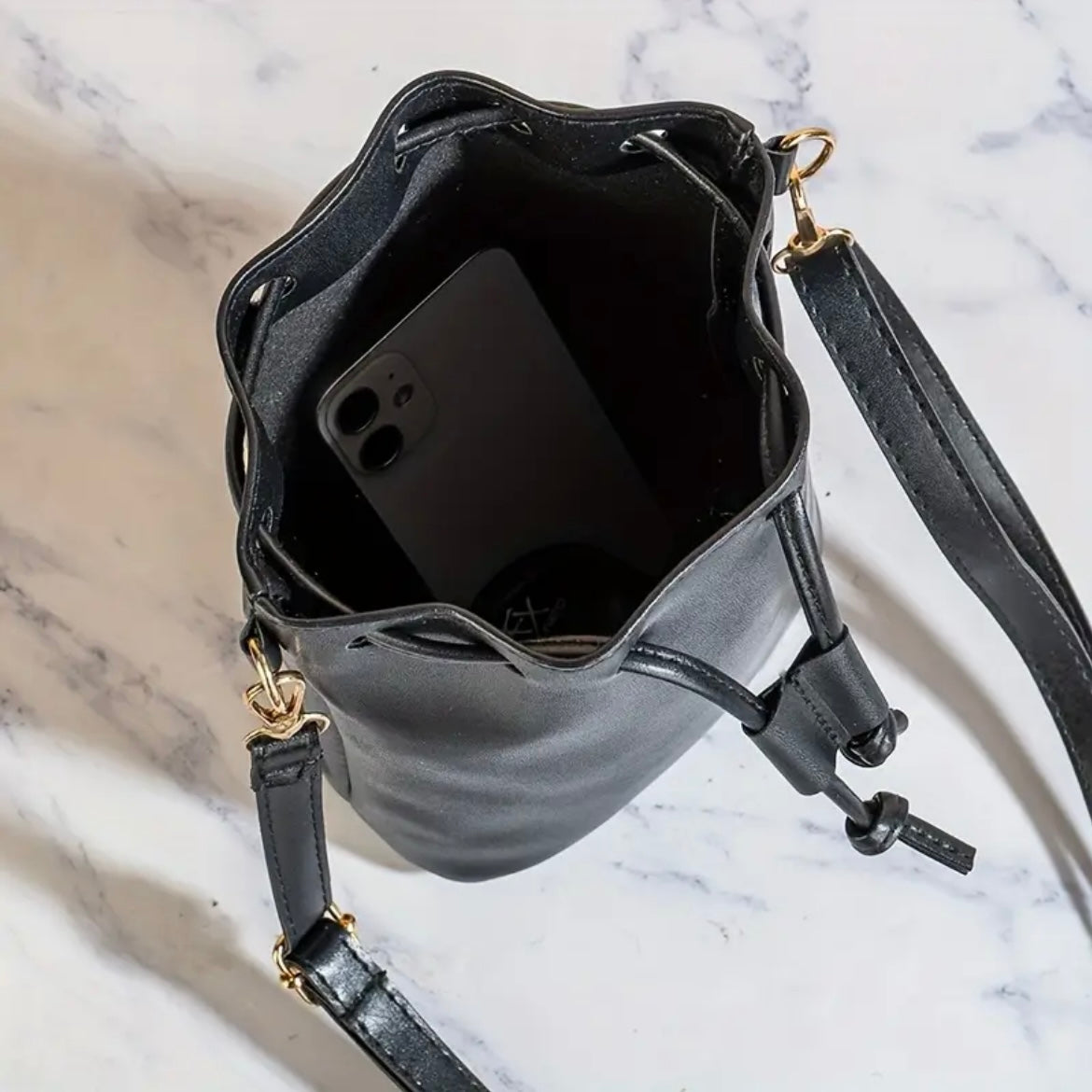 Black leather handbag with a phone inside on a marble surface