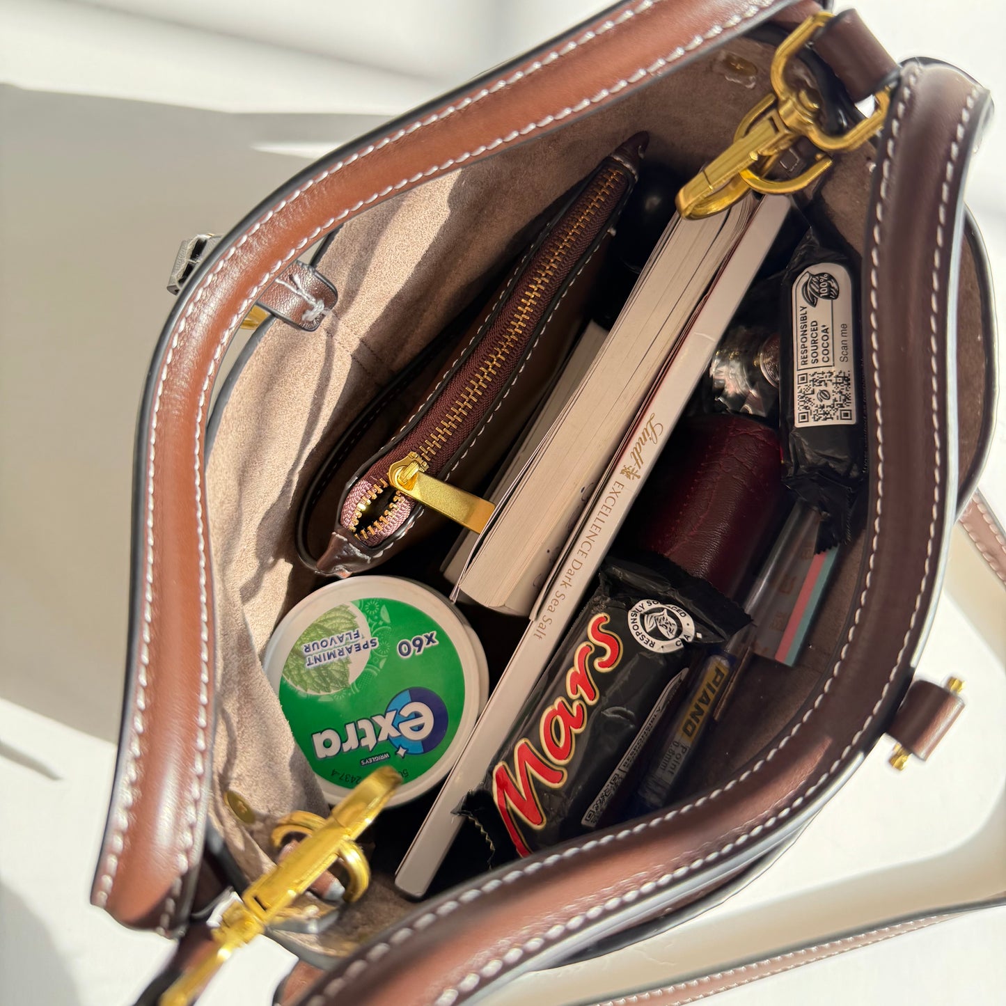 Open brown leather handbag with various items including a book, candy, and stationery.