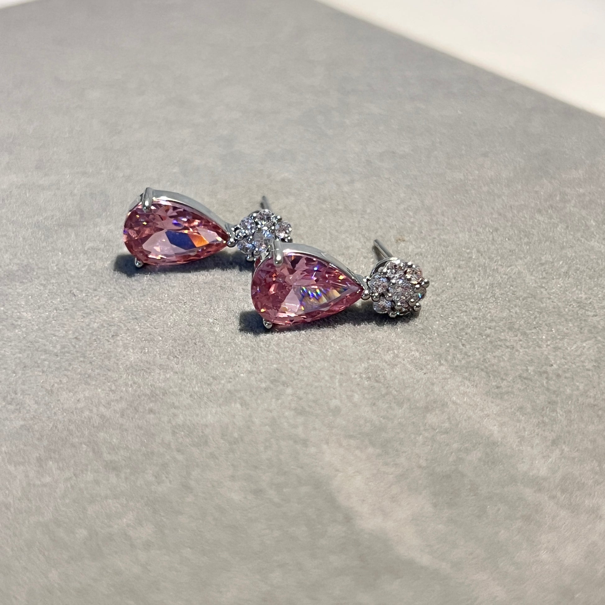 Pair of pink teardrop earrings with silver settings on a gray surface